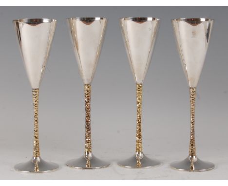 A set of four silver wine goblets by Stuart Devlin (1931-2018), each of plain conical form, raised on naturalistic gilt stems