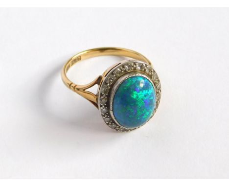 OPAL RING. An 18ct. gold & platinum, black opal & diamond ring. The cabochon opal set within a diamond border, comprising eig