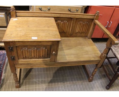 An English reproduction oak finished telephone table with linen fold carved panel back and single cupboard door 