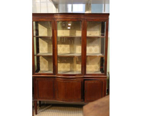 A first quarter 20th century mahogany finished display unit having chip carved frieze bowed glazed central section flanked by