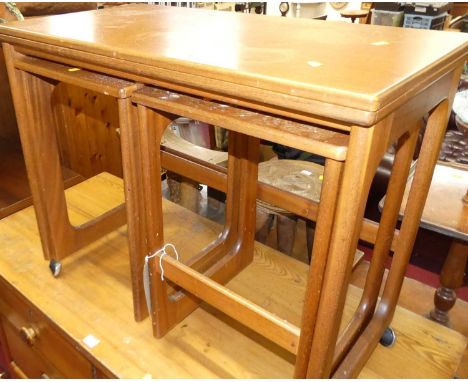 A 1970s teak nest of three occasional tables, the larger table having fold-over surface and on roller castors, width 76cm