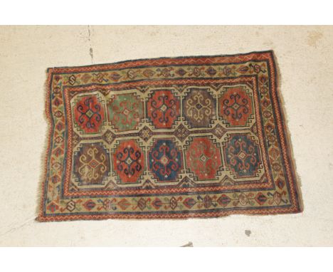 A Caucasian rug, the centre field with two rows of five medallions in madder, pale red, green blue and cream on a cream diamo