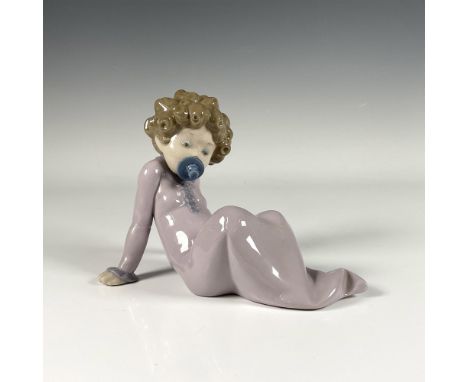 Adorable glossy figure of a baby with curly hair biting a pacifier and sitting on the floor in serene pink pastel tones. Llad