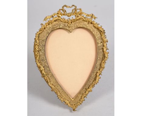 An Edwardian gilt metal easel photograph frame of heart shaped form with foliate and scroll border decoration within a raised