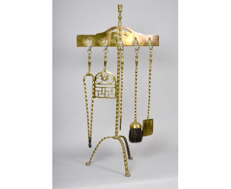 A 19c brass fire side tool rest with a central twist moulded tripod stand, pierced horizontal tool holder carrying five tools