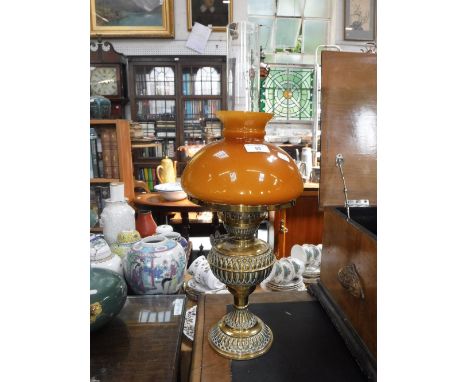 AN EDWARDIAN EMBOSSED BRASS OIL LAMP with a burnt orange glass shade