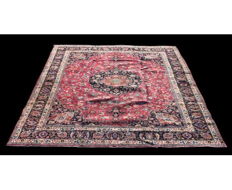 A Persian Mashad woollen hand knotted carpet with central floral medallion on a red ground, 372 by 293cms (146.5 by 115ins).