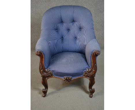 A circa 1830s mahogany tub armchair, upholstered in striped blue fabric, with a button back, the carved scrolling arms decora