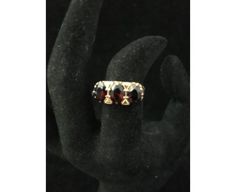 A 9ct yellow gold dress ring, set with three oval red stones, probably garnets, within a row of graduated heart form filigree