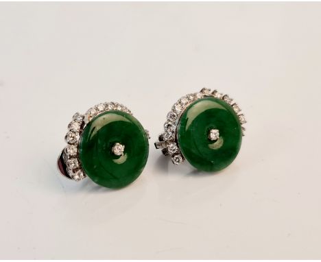 A pair of jadeite jade and diamond earrings each set with a circular piece of jadeite half surrounded by round brilliant cut 