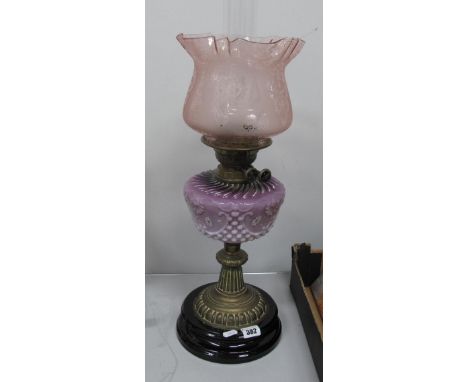 An Oil Lamp, circa 1900 with black glazed terracotta base, lilac tinted glass well and pink shade.