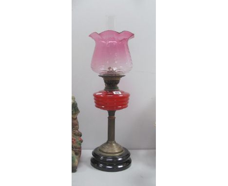 An Oil Lamp, circa 1900 with black glazed terracotta base and red glass well, with cranberry shade.