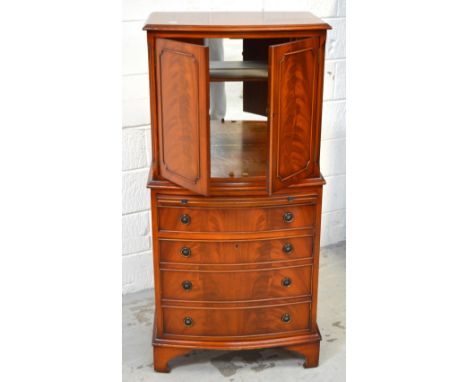 A reproduction flame mahogany drinks cabinet set above a flight of four drawers, bow front with a mirrored interior and singl