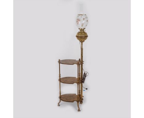 A brass table lamp with three legs and three shelves decorated with foliage patterns. The lamp extends from the base above th