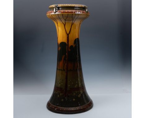 A round pedestal in brown, green, and orange depicting the woodlands at sunset, with black silhouettes of trees and others st