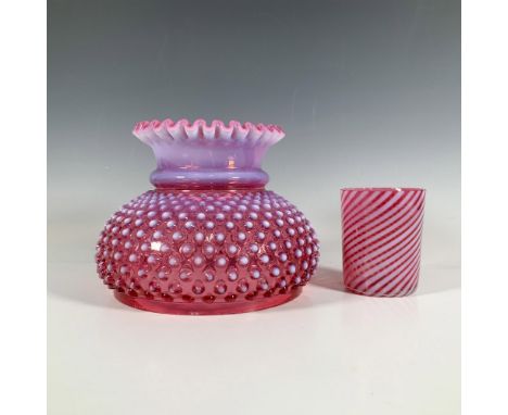 A cranberry colored glass lamp shade with a round body adorned with a hobnail high relief pattern, a lavender neck, and a wav