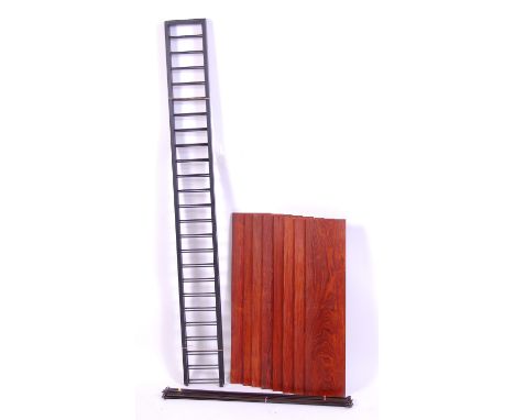 A 1970s Ladderax enamelled metal and teak two-division wall shelf, comprising twelve shelves, three laddered uprights, with d