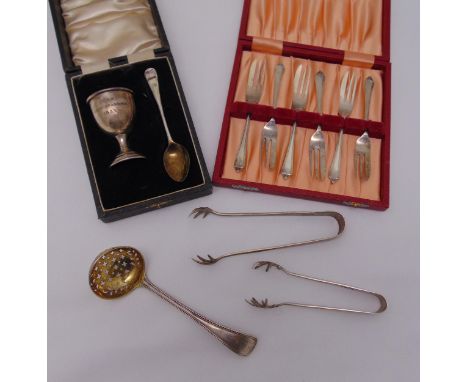 A hallmarked silver eggcup and spoon in fitted case, a cased set of pastry forks, two pairs of ice tongs and a caddy spoon, a