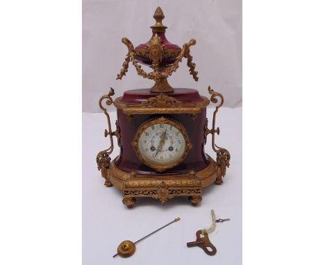 A French gilded metal and porcelain oval mantle clock, white enamel dial with Arabic numerals, surmounted by a vase with gild