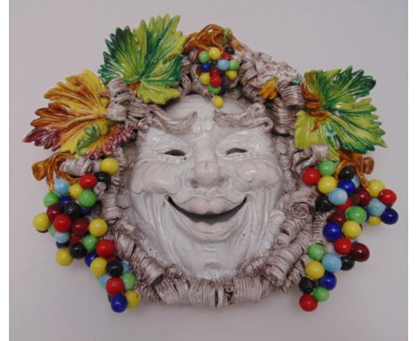 An Italian ceramic Majolica wall plaque in the form of a masked jester with leaf and berry surround, 37 x 45cm