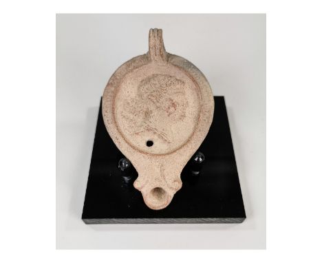 Ca.200 AD. An earthware oil lamp with a flat base, heart-shaped nozzle, and triangular lug handle; radiating tongue-shaped pa