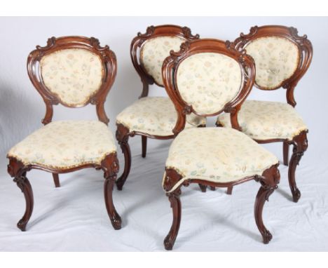 A set of four Victorian walnut dining chairs with oval scroll carved backs inset floral print upholstered panels, on scroll s