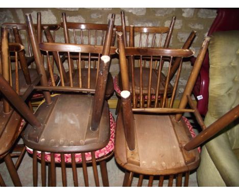 A set of eight Ercol style stained beech wood stick back kitchen chairs with dished laminated plywood seats raised on simple 