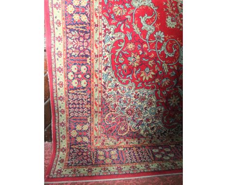 A large wool carpet, the deep red field interspersed with foliate and floral decoration, and set within a further foliate bor