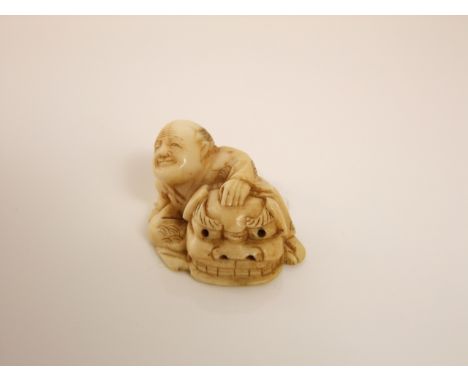 A small ivory netsuke of a crouching man with a dragons mask