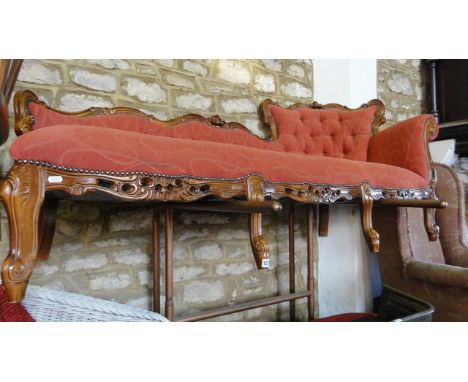A reproduction chaise lounge/couch with upholstered seat and button back within a flamboyant show wood frame