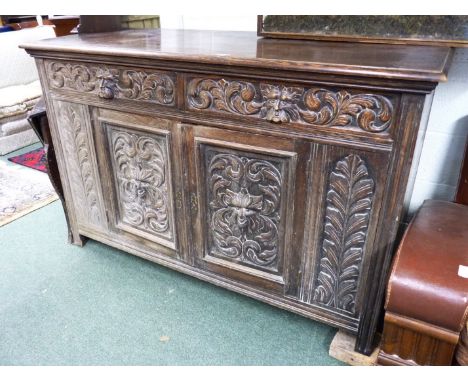 A heavily carved Victorian oak sideboard.  Fitted pair of scroll and "green man" carved doors enclosing fitted shelf, two nar