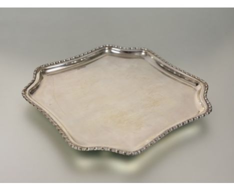 An Edwardian silver salver, Atkin Brothers, Sheffield 1910, of shaped square form, with bead and reel rim and raised on shape