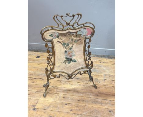 A mirrored brass firescreen in the Art Nouveau taste, c. 1900, the cartouche-shaped bevelled mirror plate enamel-painted with