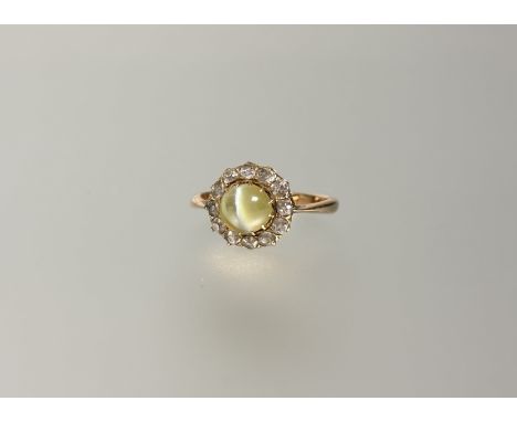 An 18ct gold cat’s eye chrysoberyl and diamond cluster ring, early 20th century, the cabochon chrysoberyl claw-set within a b