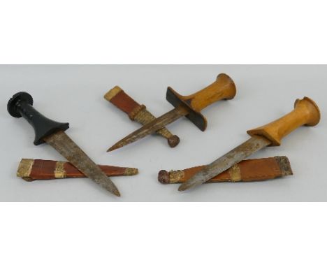 Three tribal daggers, each with two sided steel blade, hardwood grip and leather/reptile skin covered scabbard, longest 25..5