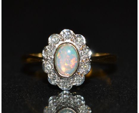 A new opal and diamond cluster ring, central oval creamy white opal, flashing red, green, purple and blue colour play, surrou