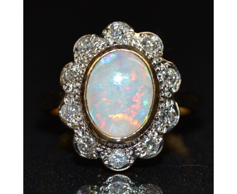 A new opal and diamond cluster ring, central oval creamy white opal, flashing red, green, purple and blue colour play, surrou