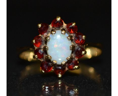 An opal and garnet cluster ring, central oval opal, flashing green,red and blue colour play, surrounded by a band of ten red 