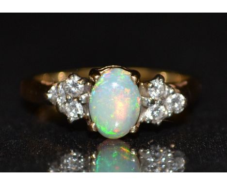 An opal and diamond cluster ring, central oval opal, flashing green, red and blue colour play, flanked to each side by a tria