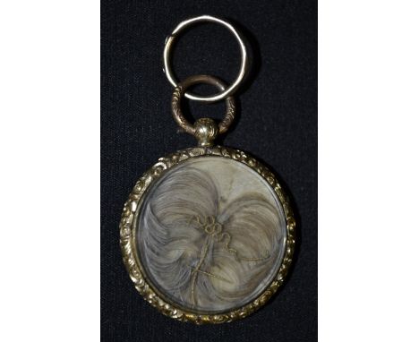 A George III mourning pendant, glazed hair work aperture front, engine turned and black onyx inlaid reverse, embossed floral 