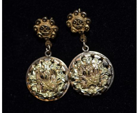 A pair of Mayan/ Aztec yellow metal earrings, triple-layered gold ring drop, suspended from a mask head pin, threaded pillar,