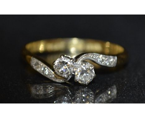 A two stone diamond twist ring, two round brilliant cut diamonds twist set between tapering diamond accented shoulders, total