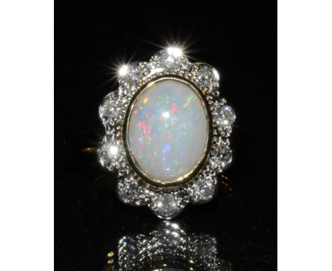 A new opal and diamond cluster ring, central oval creamy white opal, flashing red, green, purple and blue colour play, surrou