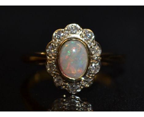 A new opal and diamond cluster ring, central oval creamy white opal, flashing red, green, purple and blue colour play, surrou