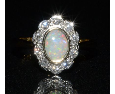 A new opal and diamond cluster ring, central oval creamy white opal, flashing red, green, purple and blue colour play, surrou