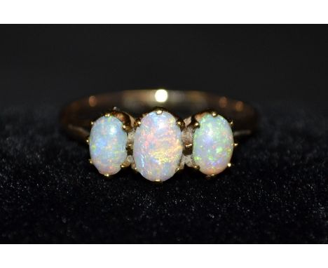 An opal three stone trilogy ring, central oval opal, flanked to each side by a smaller opal, all flashing, orange, red, green