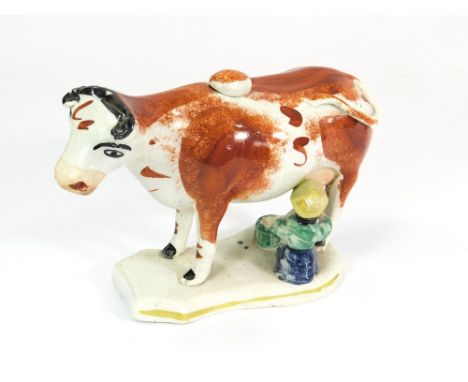 COW CREAMER. A 19th century cow creamer, the cow decorated in rust & black with a seated milk maid beneath. Lid intact. Heigh