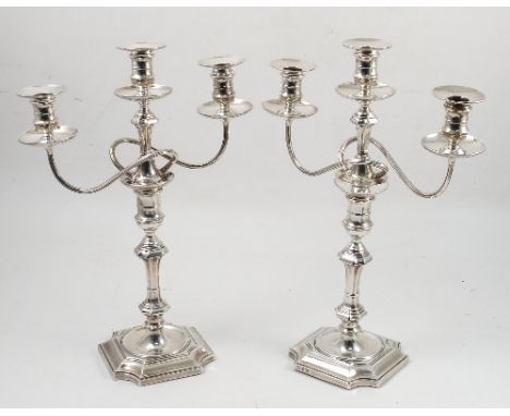 A pair of silver three light candelabra, in the Georgian style, with separate sconces, scrolling arms and typical column, rai