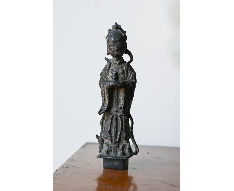 An antique Chinese bronze figure of Guanyin, the age patinated surface with traces of reddish enamels, standing on a square s