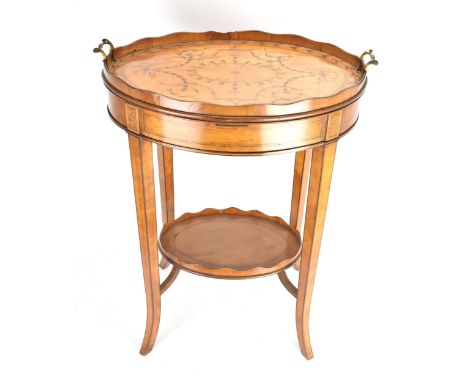 An Edwardian satinwood two tier table, having an oval top with twin carrying handles and inlaid with Sheraton Revival inlaid,